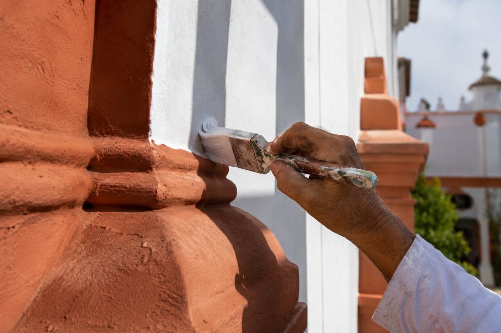 Detalle de mano experta aplicando pintura blanca con brocha sobre paramento terracota