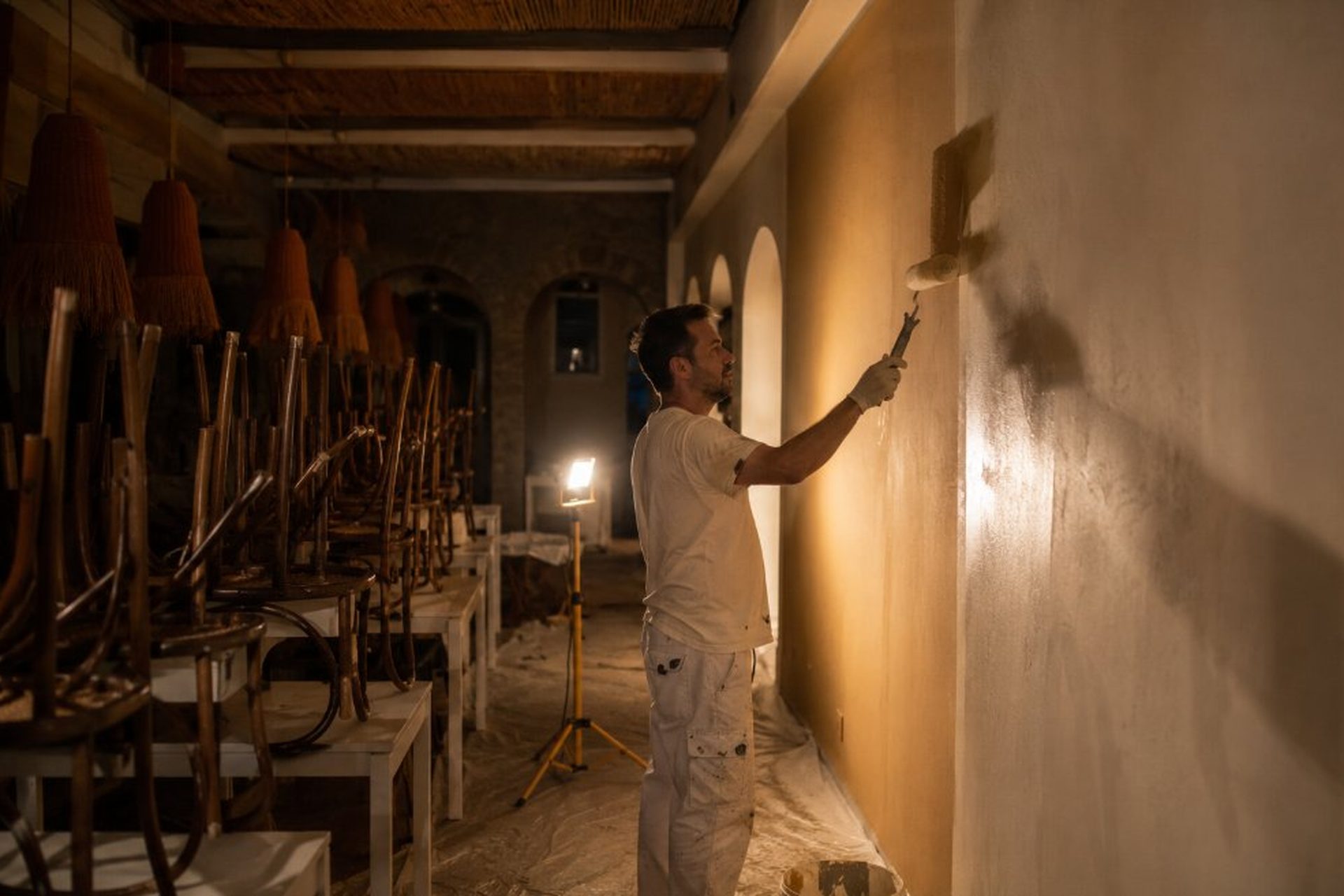 Pintor profesional trabajando de noche en restaurante cerrado con sillas apiladas y luz de trabajo