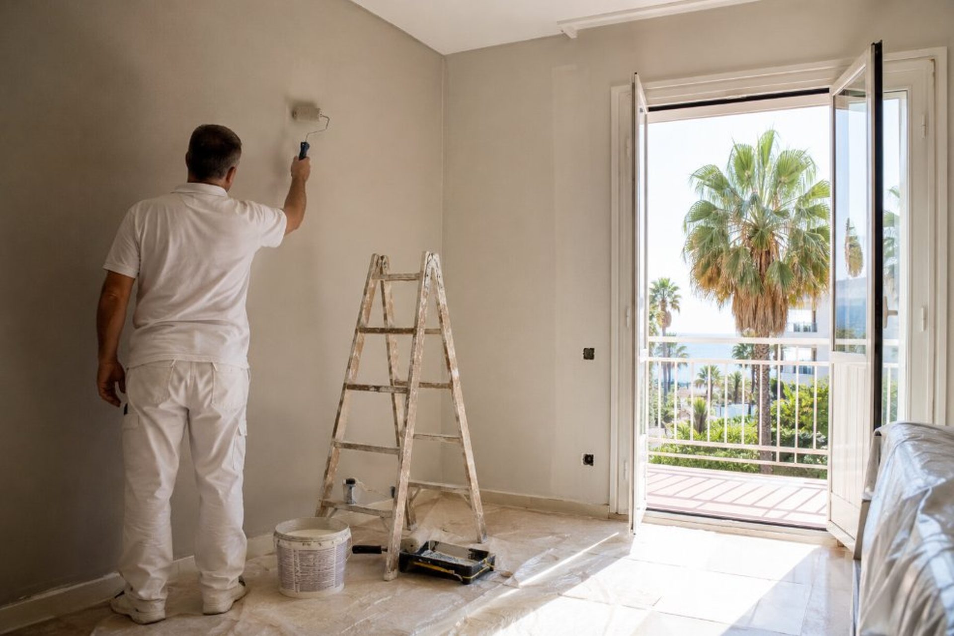 Pintor profesional en apartamento turístico de La Pineda con balcón abierto y vista a palmeras y mar Mediterráneo