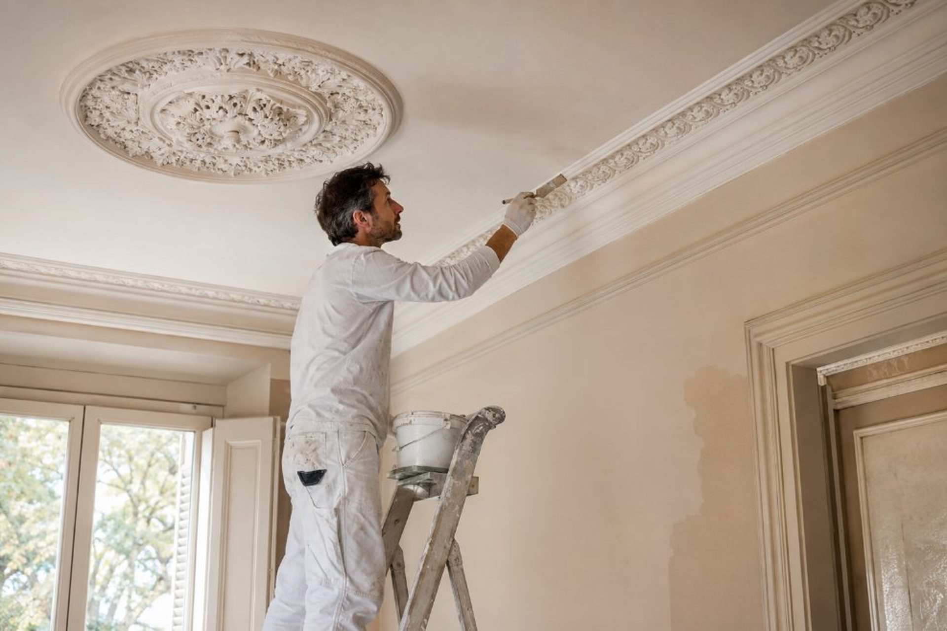 Pintor restaurando moldura modernista de techo con roseta floral decorativa en vivienda del Eixample de Reus